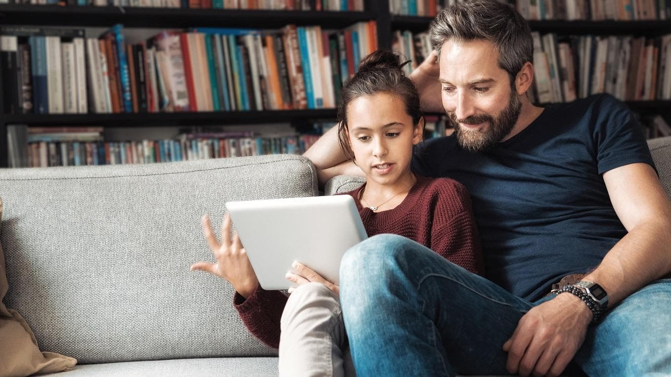 happy father and daughter having fun with digital tablet on couch